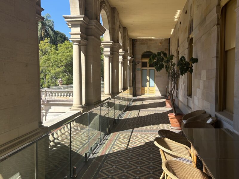 Arched sandstone colonnade with patterned tiled floor and new glass balustrade behind the heritage balusters.