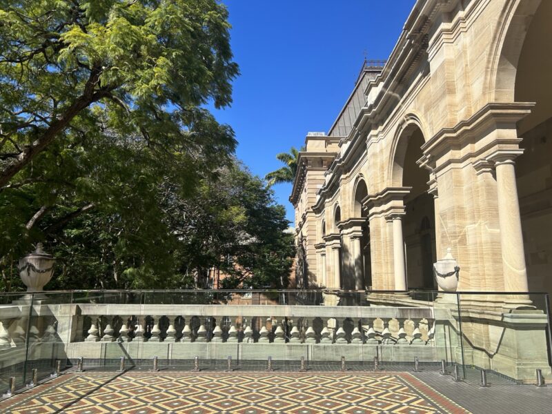 Balcony edge with glass balustrade, sandstone arches and jacaranda canopy.