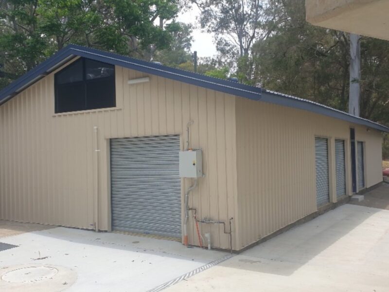 Repaired canoe shed with beige cladding, navy roof, clerestory glazing and roller doors on a new concrete apron.