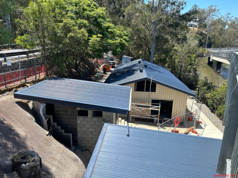 Aerial view of the amenities block under construction beside the canoe shed, with treed riverbank.