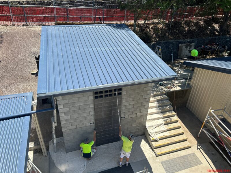 Two workers finishing the blockwork entry of the amenities block from above.