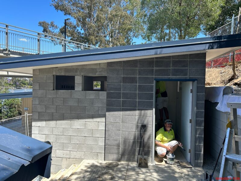 Painter working in the doorway of the newly built blockwork amenities with the river path behind.