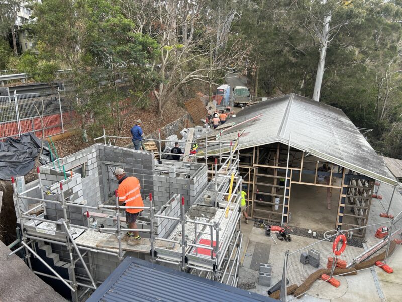 Blocklayers on scaffold building the amenities block walls next to the canoe shed frame.