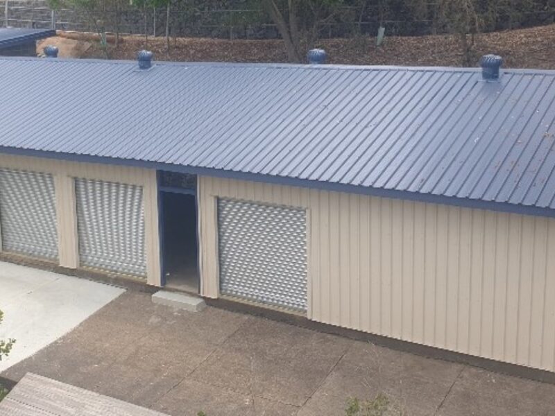 Long side of the repaired canoe shed with new navy roof sheeting and three roller doors.