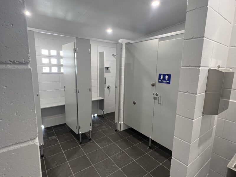 Interior of the new amenities with white tiled walls, cubicle partitions, dark floor tiles and accessible signage.