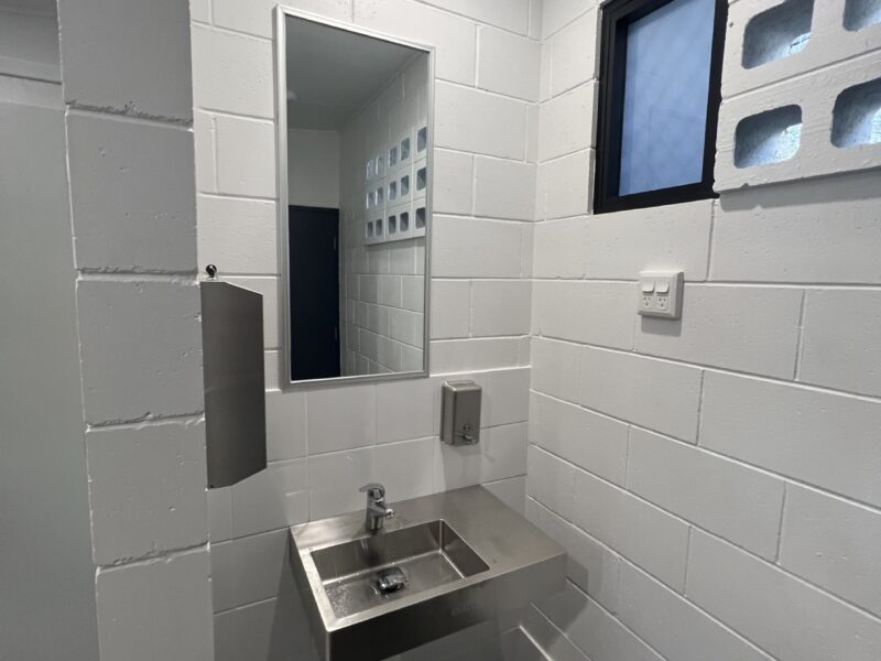 Amenities interior with stainless basin, mirror, tiled walls and breeze-block feature.