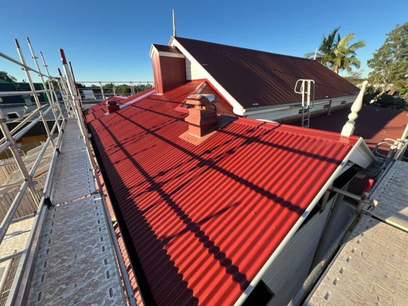 Newly sheeted red corrugated roof of Corinda Library seen from scaffold walkway in low sun.