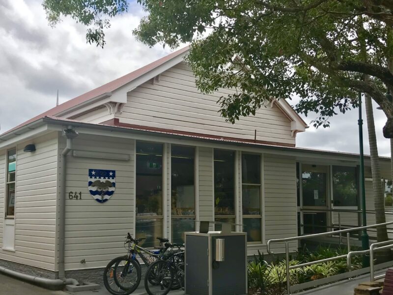 Front of the weatherboard Corinda Library with council crest, glazed entry and bikes parked outside.