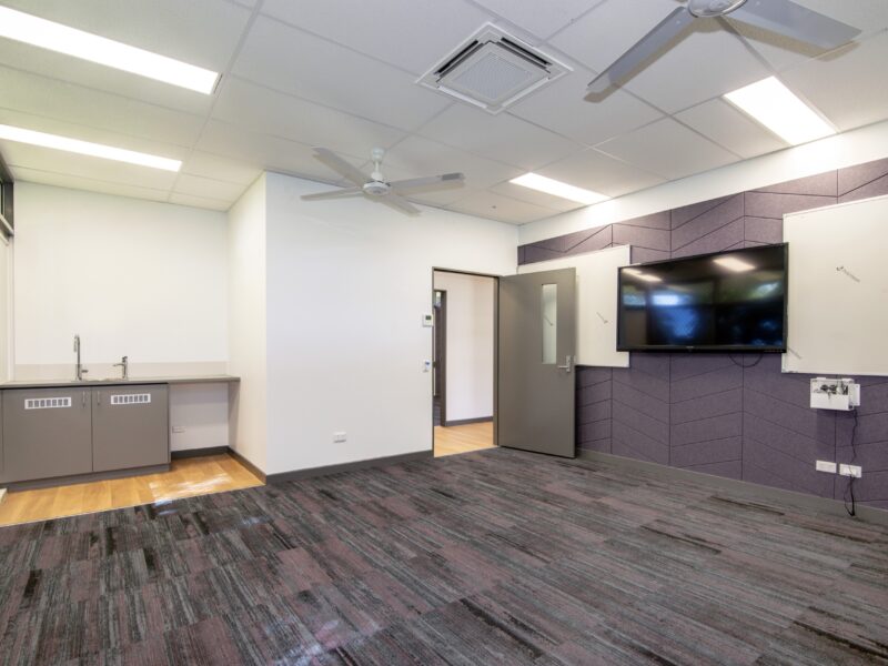 Carpeted meeting room with wall-mounted TV, whiteboard, kitchenette bench and split-system cassette AC.