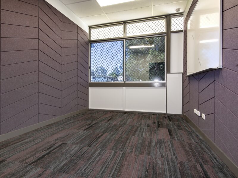 Office with herringbone purple acoustic wall panels, carpet tiles, security-screened window and wall-mounted whiteboard.
