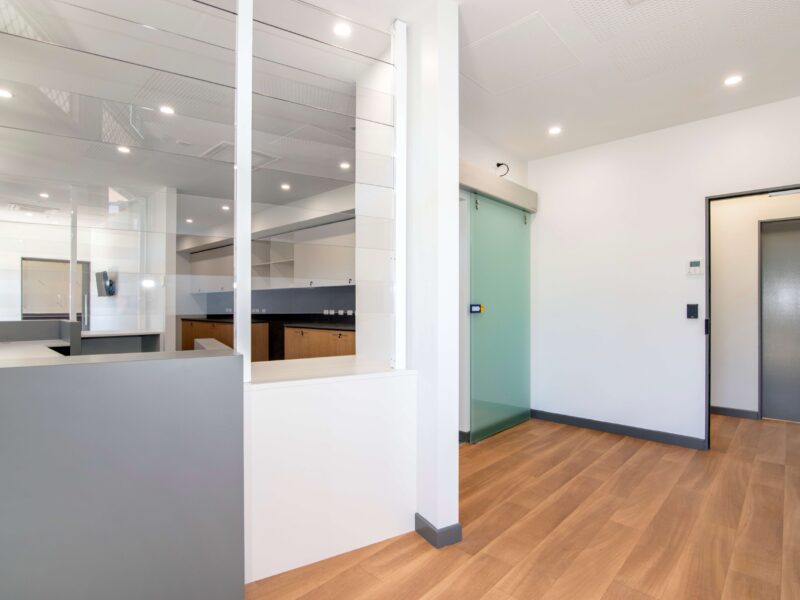 Reception area with grey counter, glazed partitions, frosted sliding glass door and timber-look flooring.