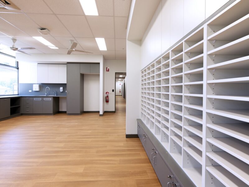 Staff room with wall of white pigeon-hole mail shelving, timber-look floor and kitchenette at the far end.