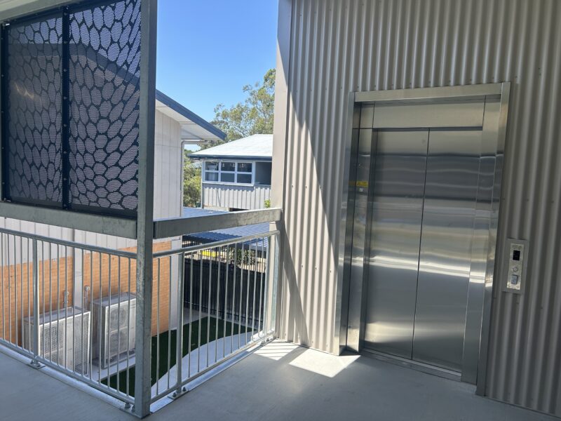 New stainless steel lift doors at upper-level walkway with balustrade and decorative screen.