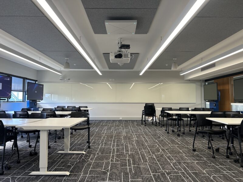 Refurbished QUT teaching space with linear LED lighting, acoustic ceiling panels, projector and collaborative desks.