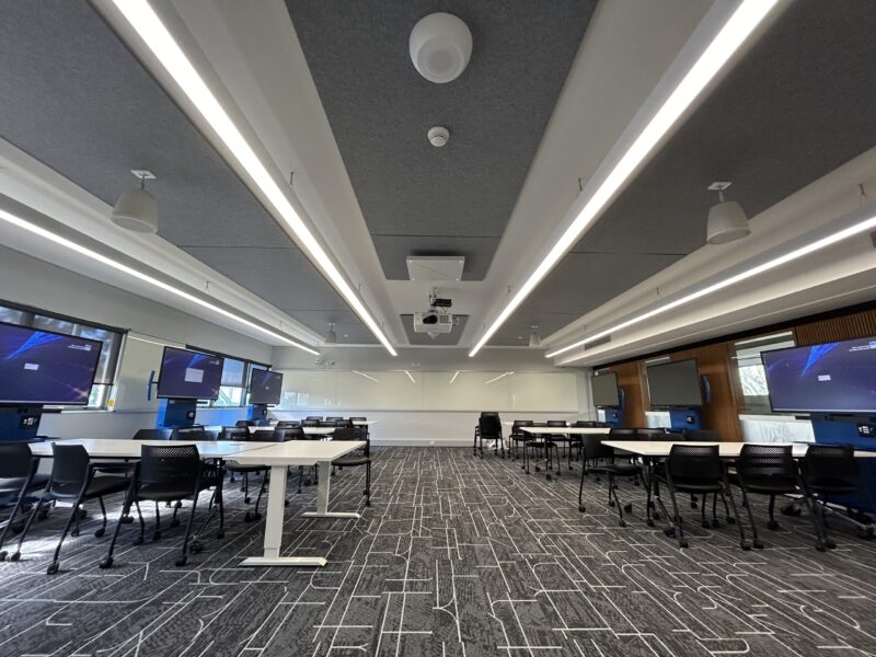 Wide view of the new learning room with screens on mobile stands, patterned carpet and linear lights.