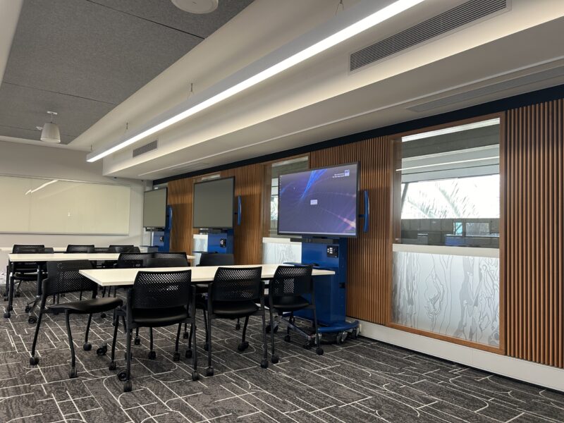 Timber-battened wall with display screens and collaborative tables in the refurbished classroom.