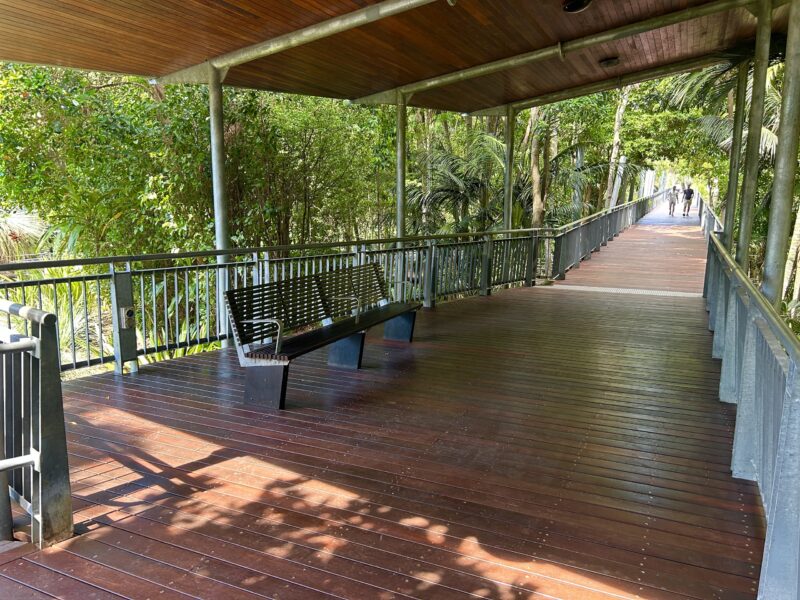 Covered rest area on the footbridge with new hardwood decking, bench seat and the boardwalk continuing into the rainforest canopy.