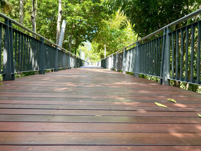 Low-angle view along freshly laid hardwood deck boards with balustrades and dappled shade from surrounding trees.