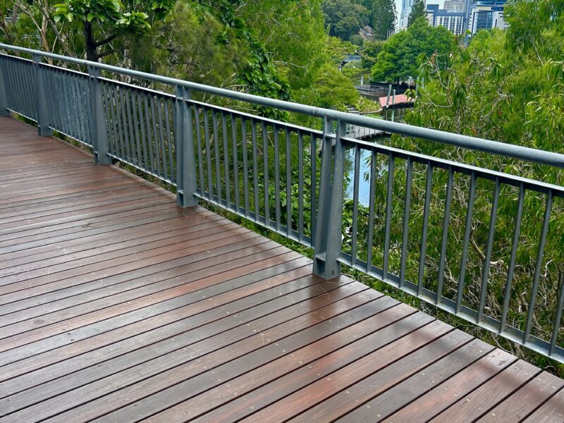 New deck boards and balustrade with Brisbane city towers visible above the tree line.
