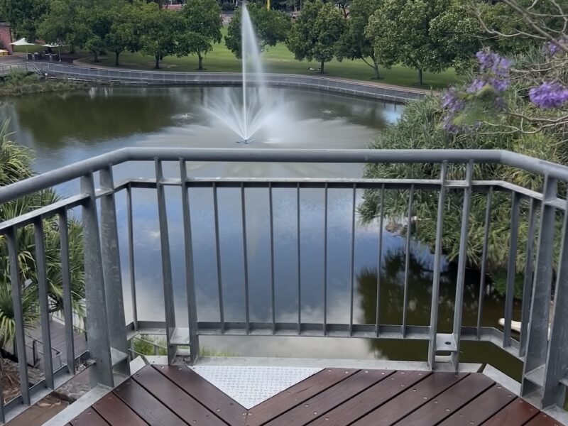 Herringbone deck lookout framing the lake fountain and apartment buildings, with jacaranda in flower.
