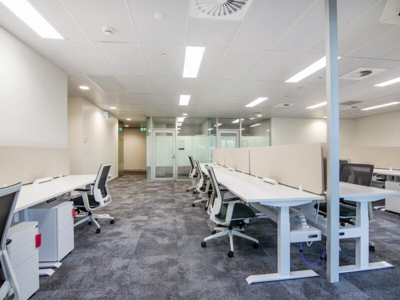 Open-plan workstation area with height-adjustable desks and linear lighting.