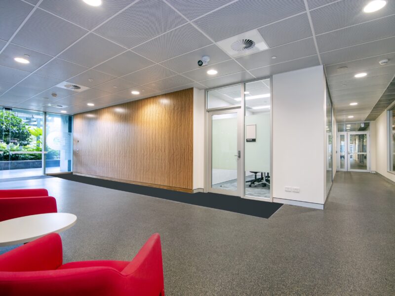 Lobby breakout with red chairs before the timber feature wall and glazed offices.