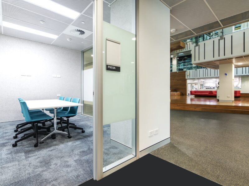 Glass-fronted meeting room with teal chairs overlooking the atrium.