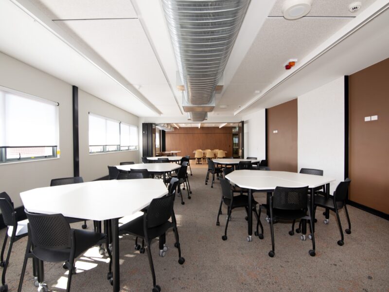 Collaborative learning space with white pod tables, black chairs and exposed circular ductwork.
