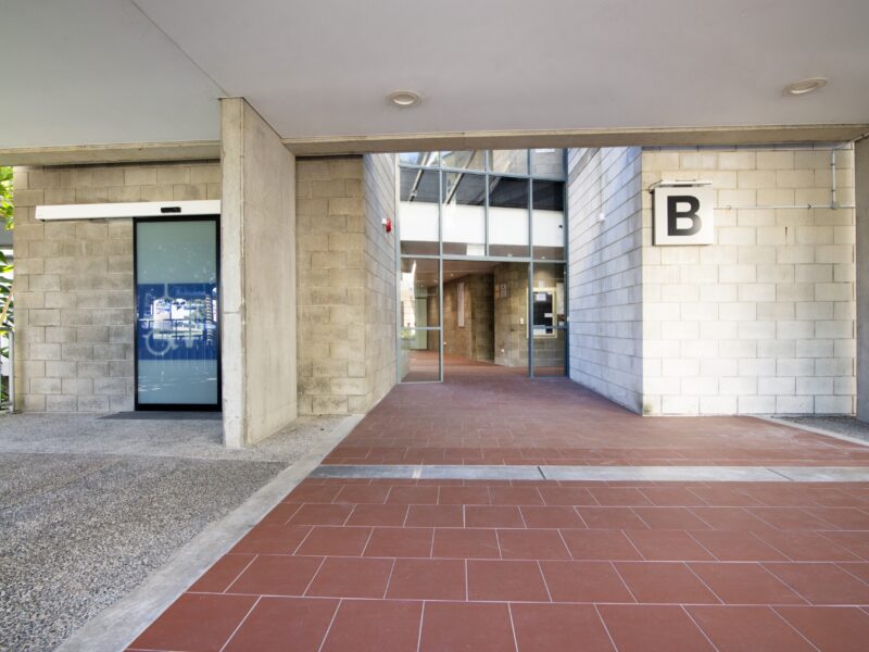 B Block ground-level undercroft entry with terracotta tile paving, blockwork walls and the B signage.