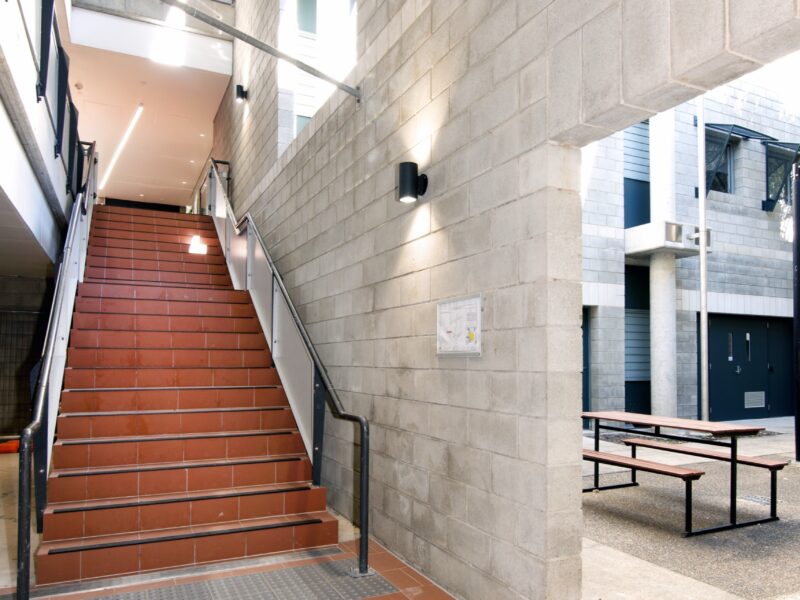 Terracotta-tiled external stair rising beside a blockwork wall to the upper levels.
