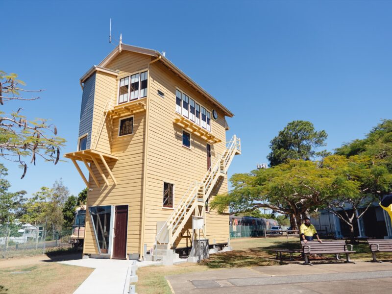 The restored Ipswich Signal Cabin at the Queensland Museum Rail Workshops, with visitors in the landscaped grounds.