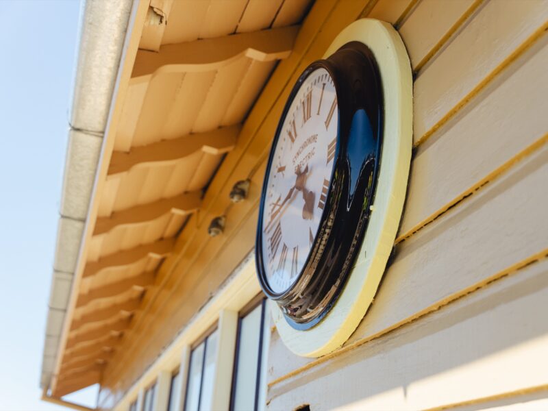 The cabin clock on the restored facade beneath the timber eaves.