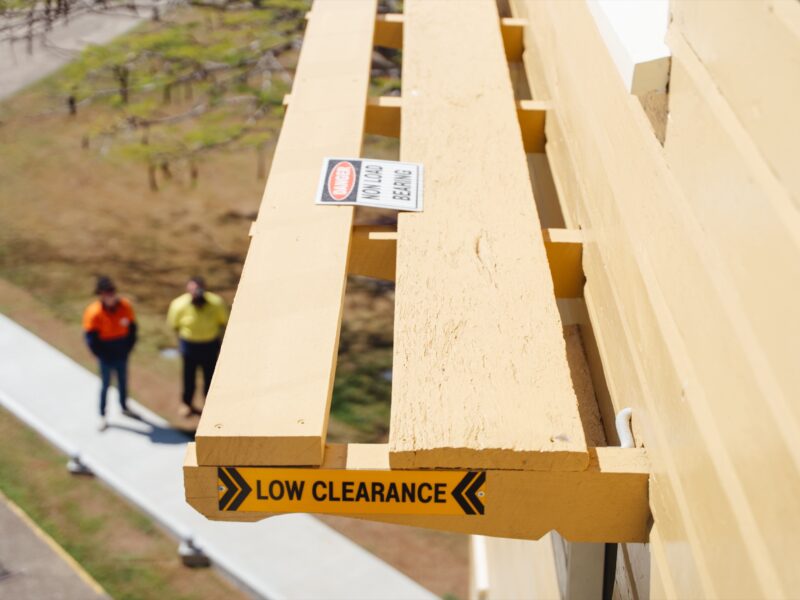 The restored balcony walkway with a low-clearance marker, visitors on the path below.