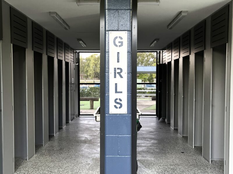 Girls amenities viewed through the open entry, with full-height partitions either side and the school grounds beyond.