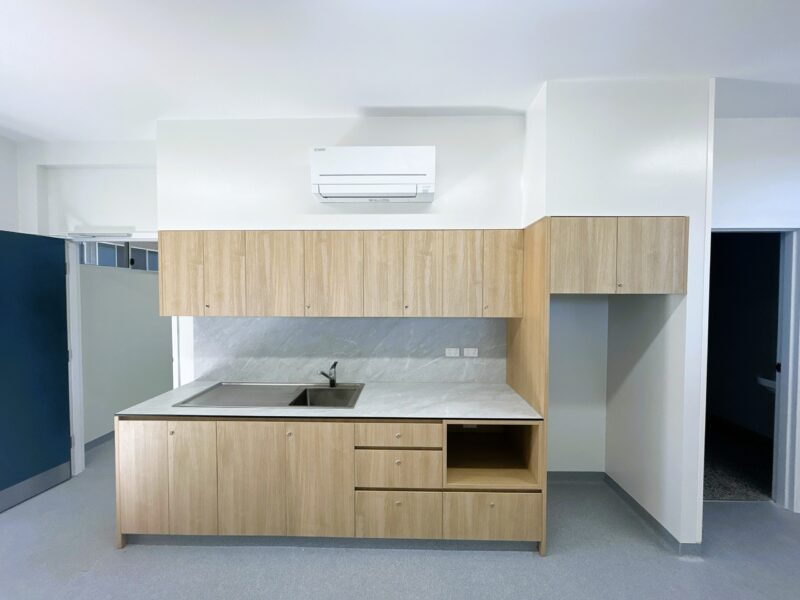 Facilities office kitchenette with timber-look joinery, stone-look benchtop and split-system air-conditioner.