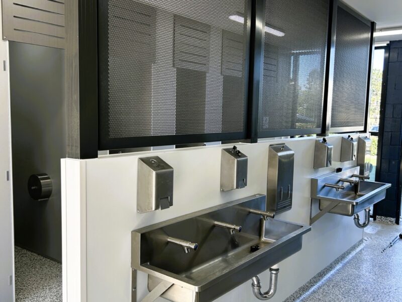 Stainless steel trough basins under mesh-screened high windows.